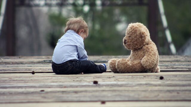 boy sitting with brown bear plush toy on selective focus photo